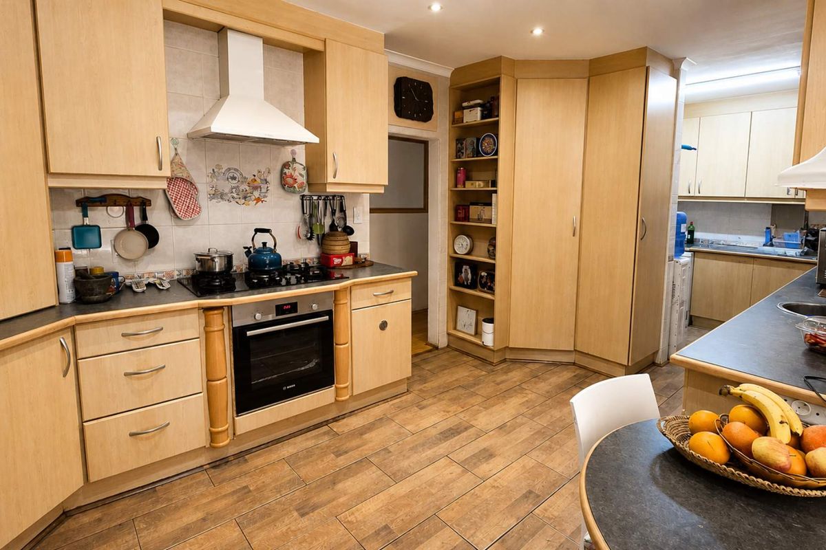 A functional kitchen featuring light wood cabinetry, built-in oven, gas hob, extractor fan, and tiled flooring with a connected scullery area.