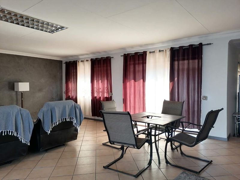 A spacious living area featuring tiled flooring, neutral walls with a dark accent wall, and large windows fitted with curtain rods.