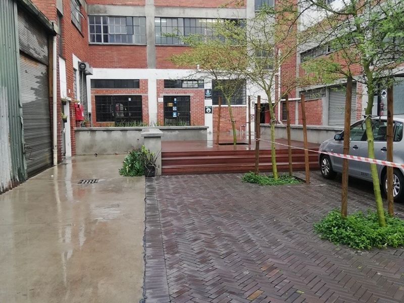 Industrial-style rear courtyard featuring exposed brick architecture, herringbone paving, timber decking, and large steel-framed windows, offering a versatile urban outdoor space.