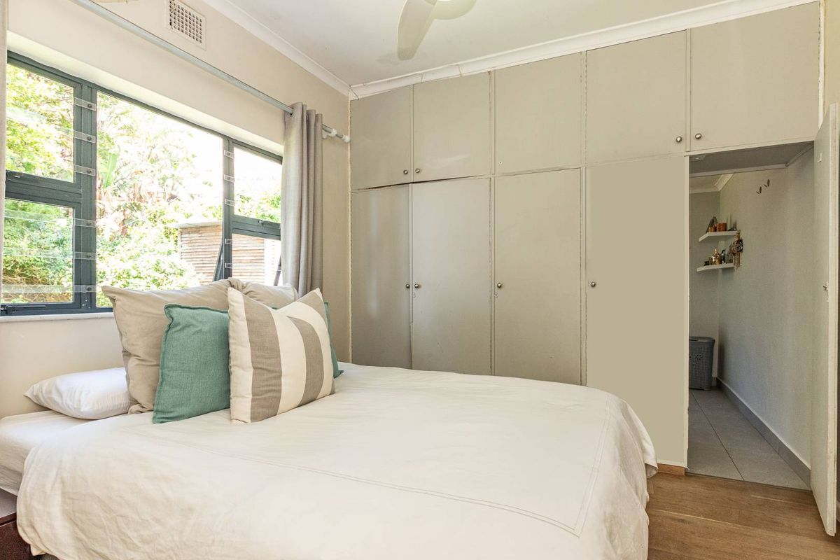 A bedroom featuring built-in floor-to-ceiling wardrobes, a ceiling fan, and a window overlooking the garden, with an adjacent walk-through area.