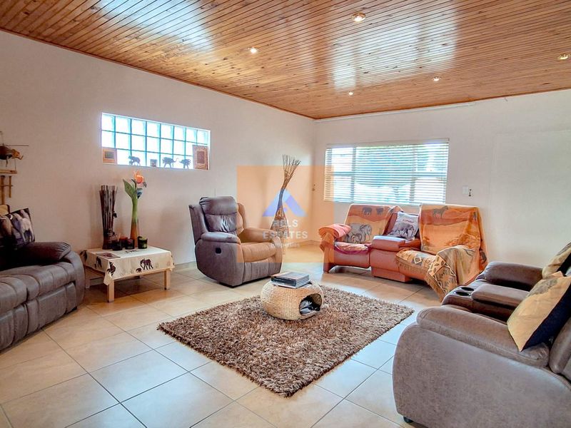 Spacious living room featuring a distinctive timber-clad ceiling, recessed downlights, tiled flooring, and a unique glass block window detail.