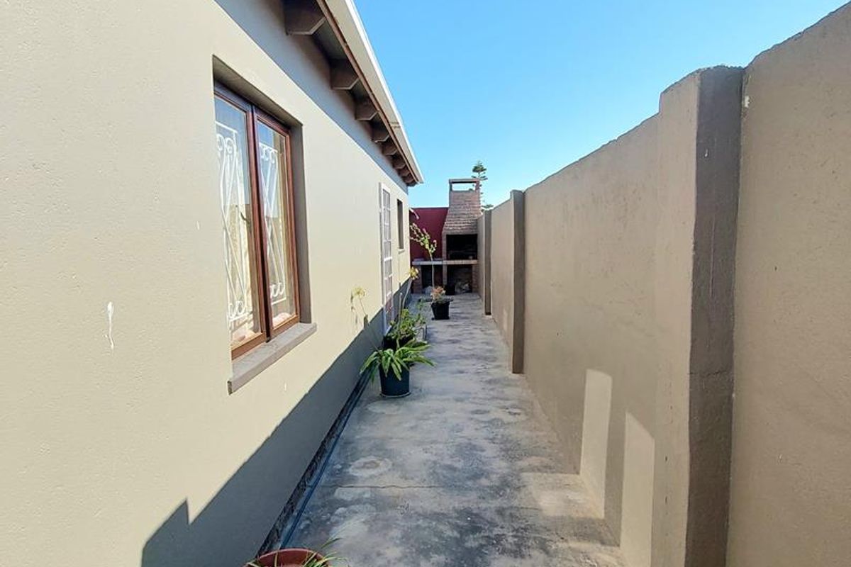 A narrow side passage featuring a concrete walkway, exterior wall access, and a built-in outdoor braai area at the rear.