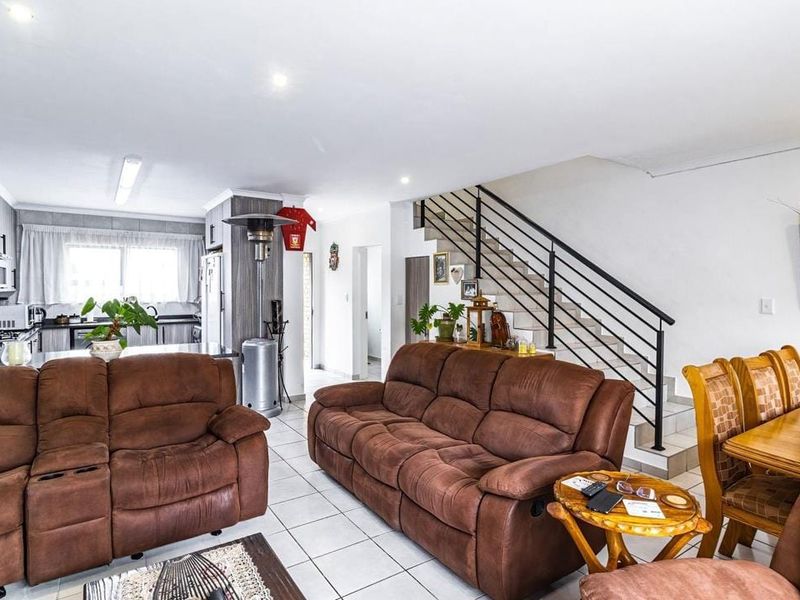 Open-plan living and dining area featuring tiled floors, recessed lighting, and a staircase with a modern metal balustrade, seamlessly connected to the kitchen.