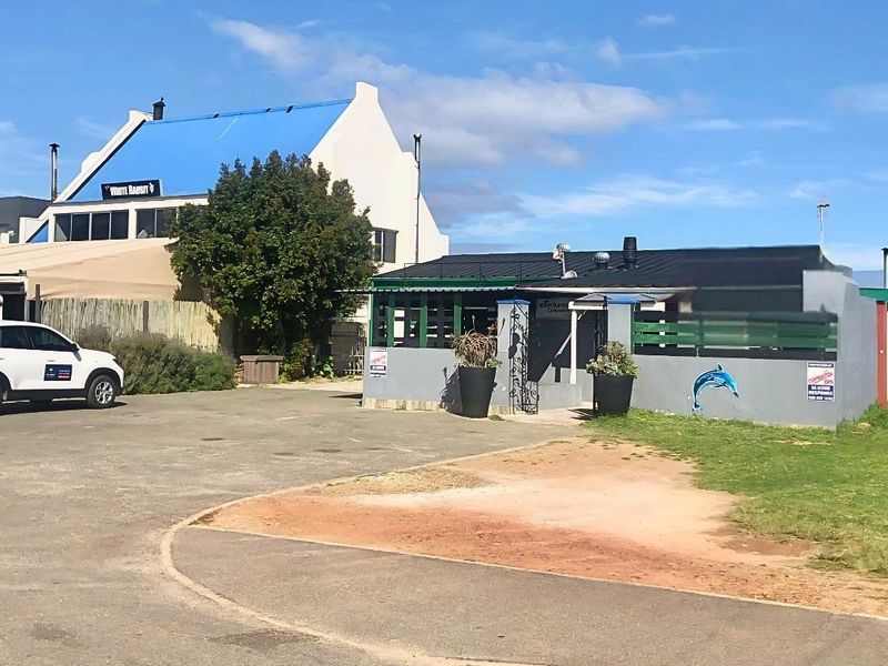 Front exterior view of the commercial property featuring a paved parking area, boundary wall, and metal roofing structure.