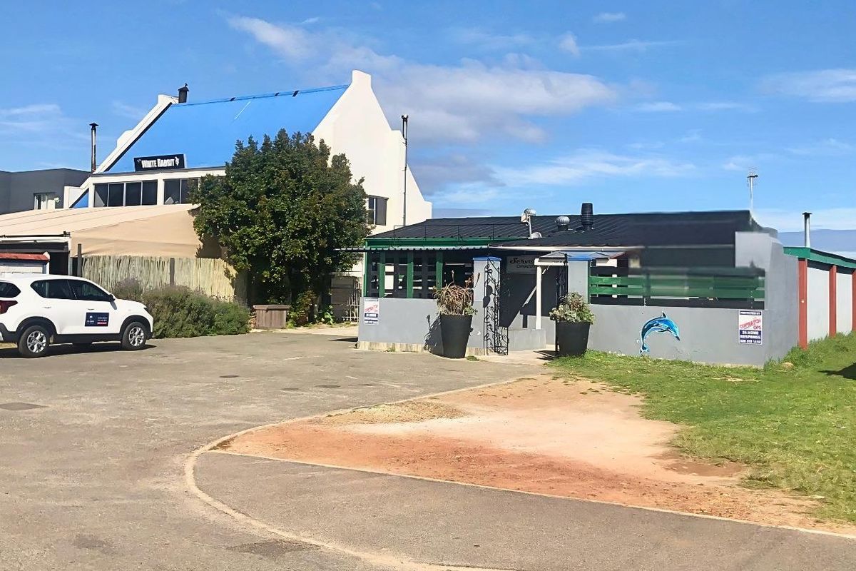 Front exterior view of the commercial property featuring a paved parking area, boundary wall, and metal roofing structure.