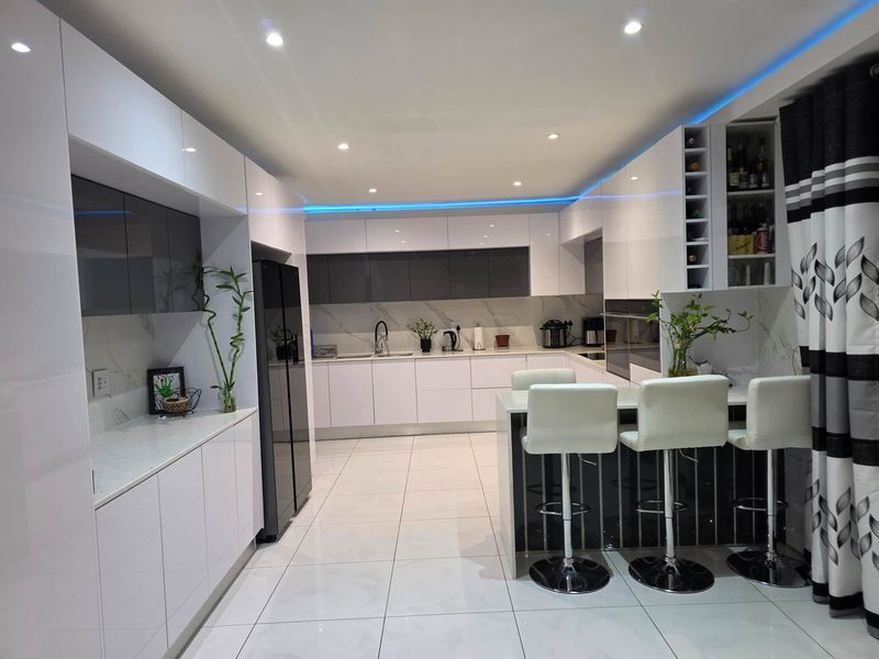 Modern kitchen featuring high-gloss cabinetry, marble-look backsplash, quartz countertops, integrated appliances, and a central island with breakfast bar seating.