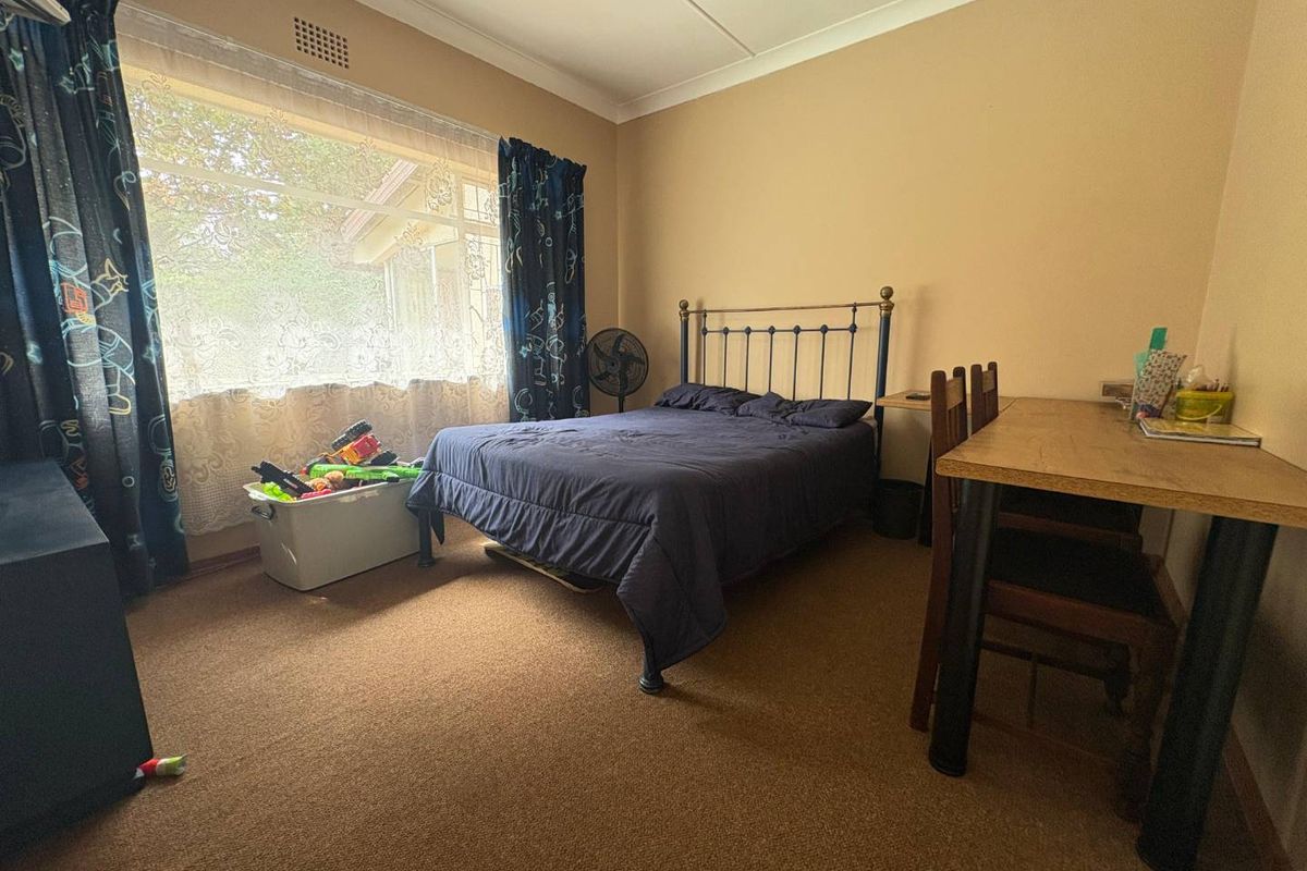 A functional bedroom featuring carpeted flooring, a large window with natural light, and standard ceiling finishes.