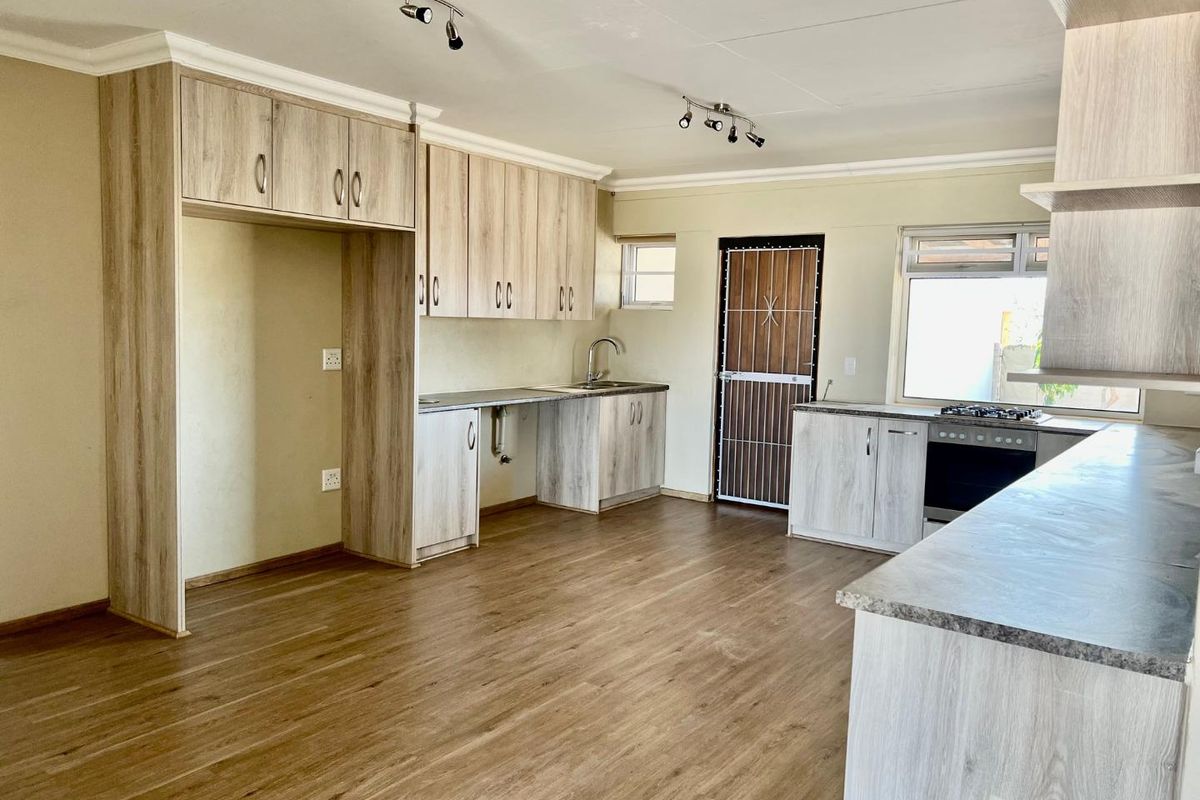 Modern open-plan kitchen featuring light wood-grain cabinetry, stone-look countertops, a built-in oven and hob, and durable laminate flooring.