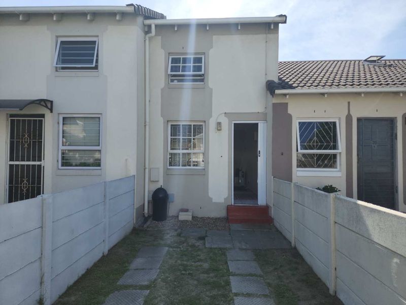 Rear view of a townhouse featuring a small garden area, paved walkway, and precast concrete boundary walls.