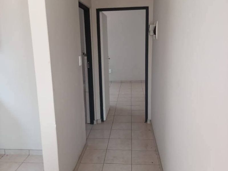 A functional, empty hallway featuring neutral ceramic floor tiles and access to adjacent rooms, providing a clean canvas for interior design.