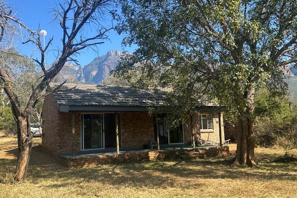 A rustic brick cottage featuring a covered patio with sliding glass doors, set against a scenic mountain backdrop.