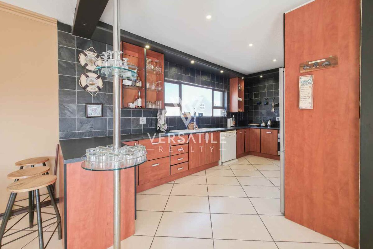 A functional kitchen featuring wooden cabinetry, dark tiled splashbacks, a breakfast bar, and tiled flooring with integrated lighting.