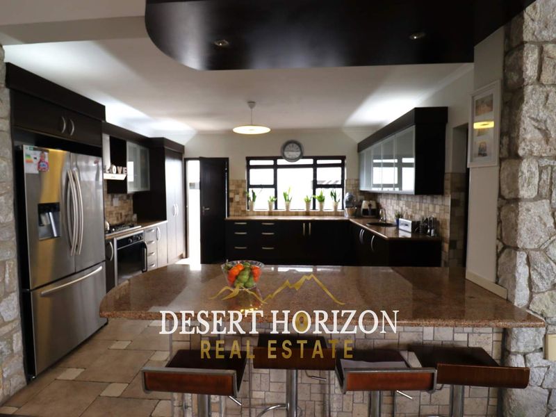 Spacious kitchen featuring dark cabinetry, granite countertops, a central breakfast bar, and stone-clad feature walls, offering a functional and modern cooking space.