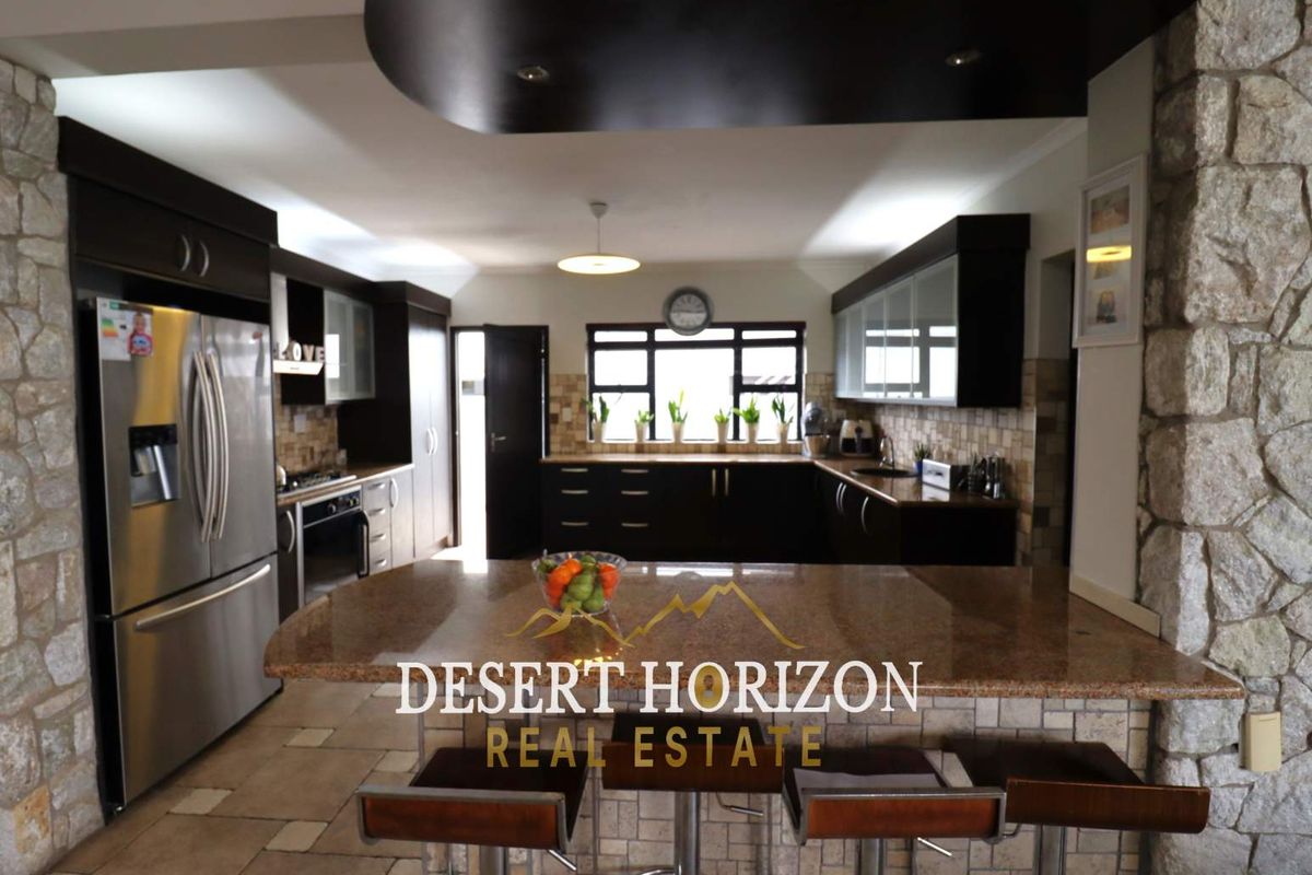 Spacious kitchen featuring dark cabinetry, granite countertops, a central breakfast bar, and stone-clad feature walls, offering a functional and modern cooking space.