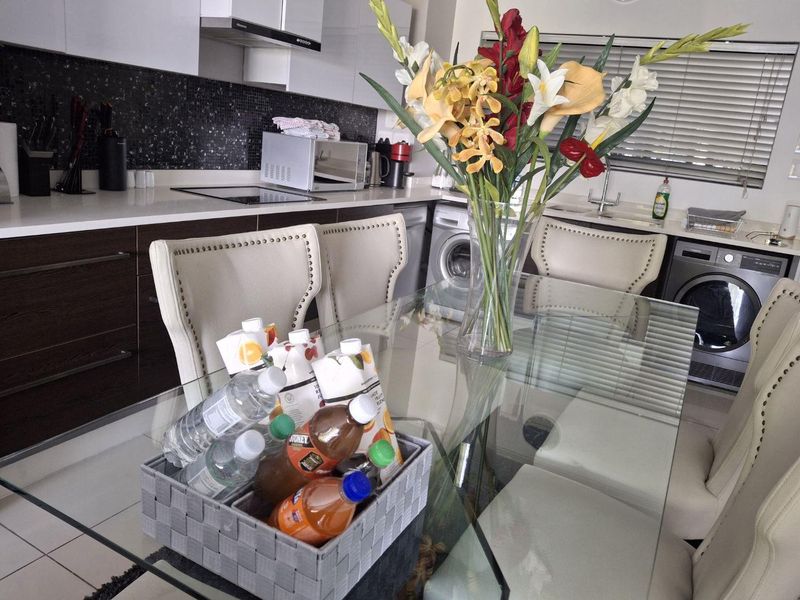 Modern open-plan kitchen and dining area featuring sleek cabinetry, stone countertops, mosaic backsplash, and integrated laundry appliances.