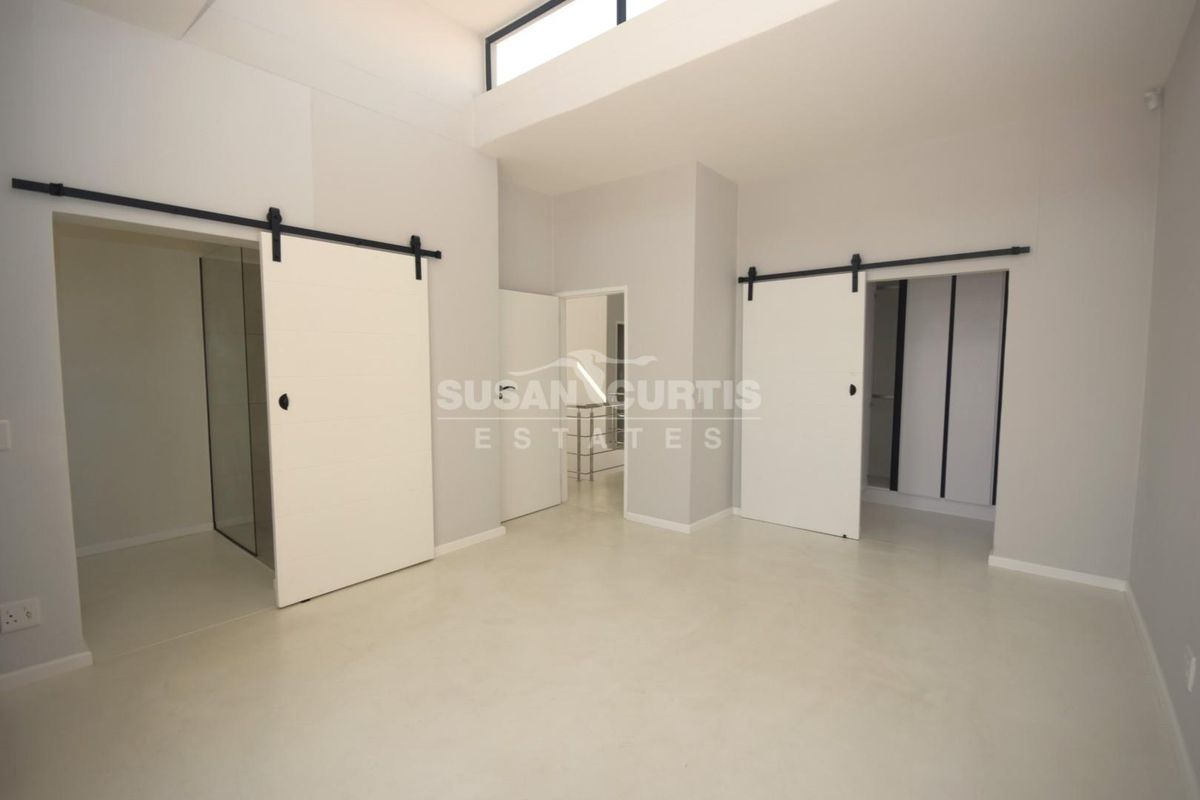 A modern, minimalist bedroom featuring polished concrete floors, high ceilings with clerestory windows, and dual sliding barn doors leading to an en-suite and wardrobe.