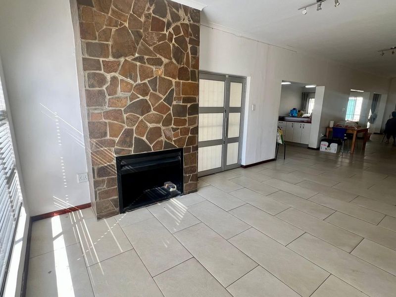 Open-plan living area featuring a prominent stone-clad fireplace, neutral tiled flooring, and a seamless transition into the adjacent kitchen space.