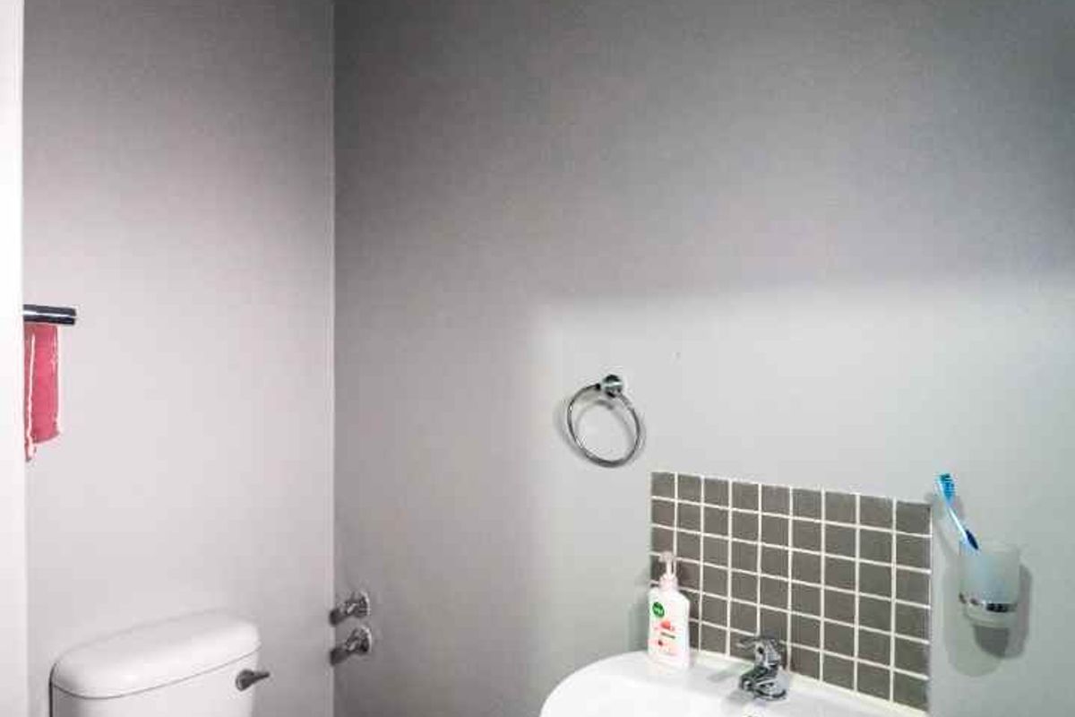 A compact bathroom featuring a pedestal sink with a tiled splashback and a standard white toilet.
