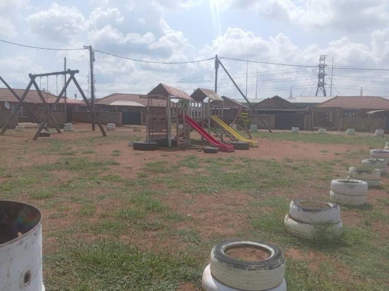 An outdoor communal garden area featuring basic playground equipment including swings and slides set within a large open space.