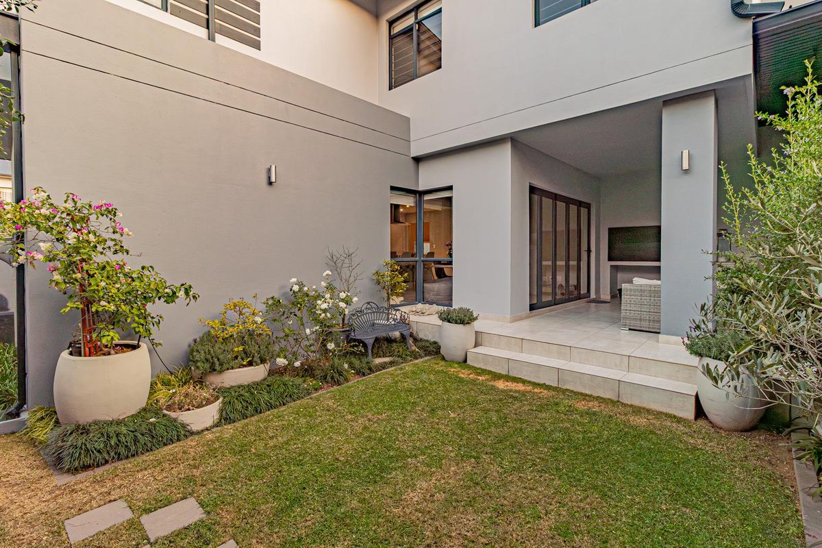 A well-maintained rear garden featuring a paved patio area, manicured lawn, and modern exterior facade with large glass sliding doors.