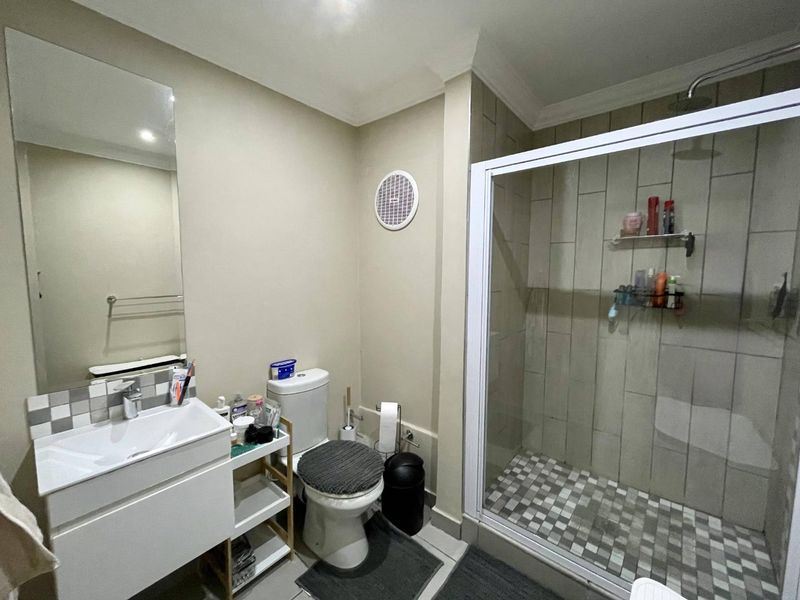 A functional bathroom featuring a modern vanity, wall-mounted mirror, toilet, and a glass-enclosed shower with tiled finishes.