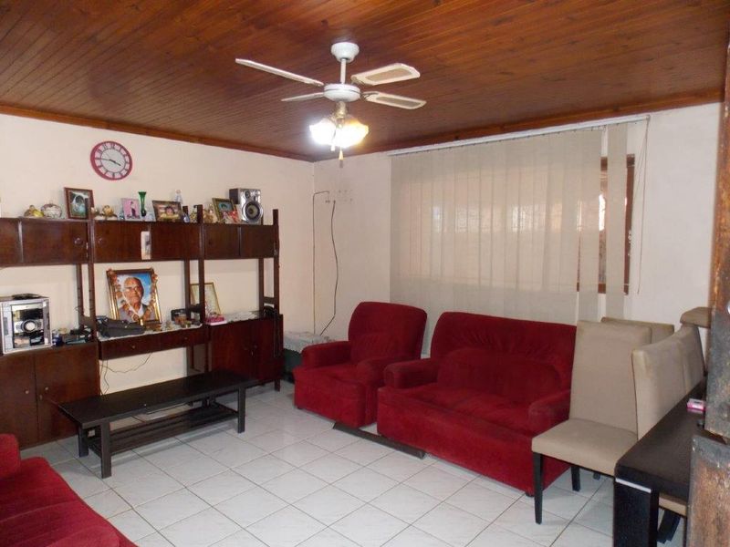 A living room featuring a timber-paneled ceiling, ceiling fan, and ceramic floor tiles, offering a functional space with neutral wall finishes.