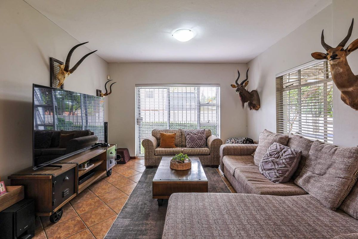 A comfortable living room featuring tiled flooring, large windows with fitted blinds, and a central ceiling light fixture.