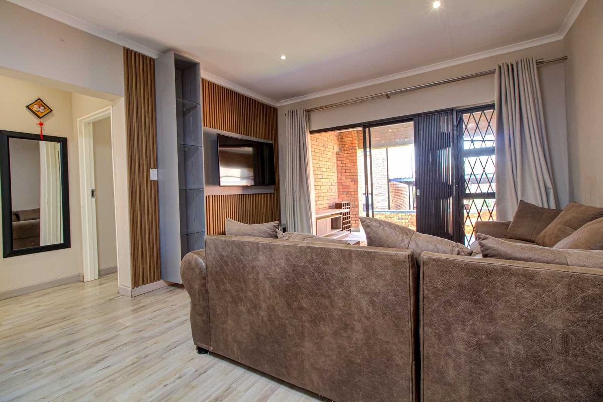 A well-maintained living room featuring modern timber slat wall paneling, recessed downlighting, and sliding glass doors leading to an outdoor patio area.