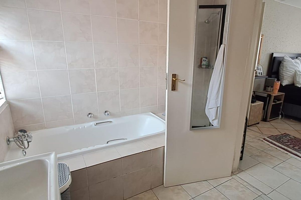 A functional bathroom featuring a built-in bathtub with tiled surround, adjacent to a bedroom area with tiled flooring throughout.