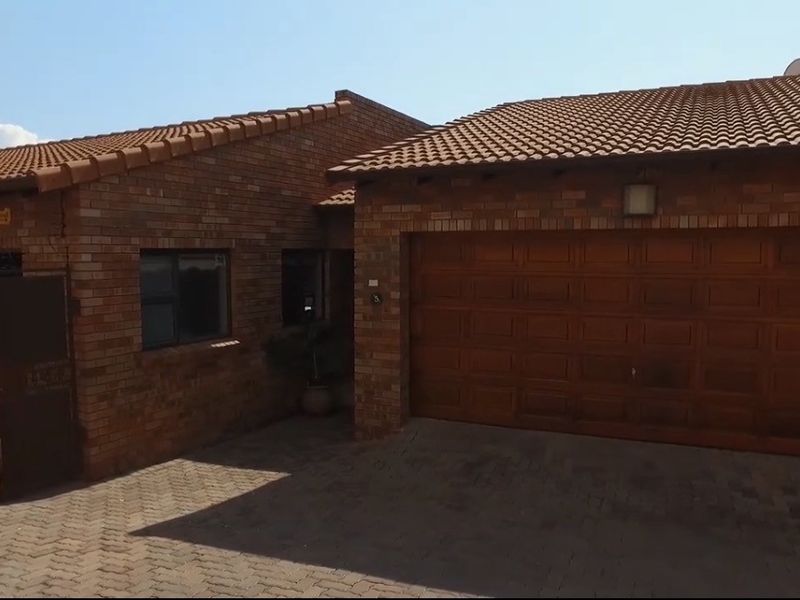 Front elevation of a face brick cluster home featuring a double garage, tiled roof, and paved driveway area.