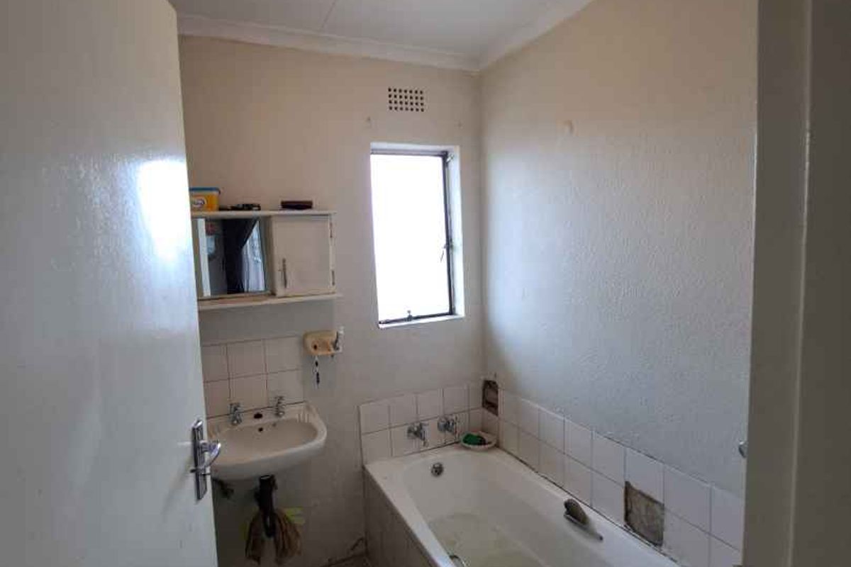 A compact bathroom featuring a bathtub, wall-mounted basin, and tiled finishes, currently requiring some maintenance and cosmetic updates.