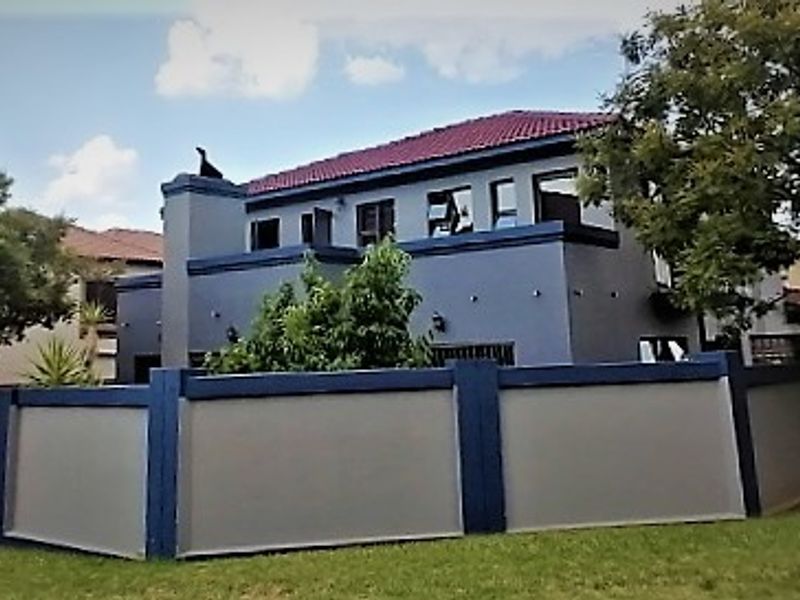 A two-story residential property featuring a tiled roof, chimney, and a secure perimeter wall, viewed from the street level.