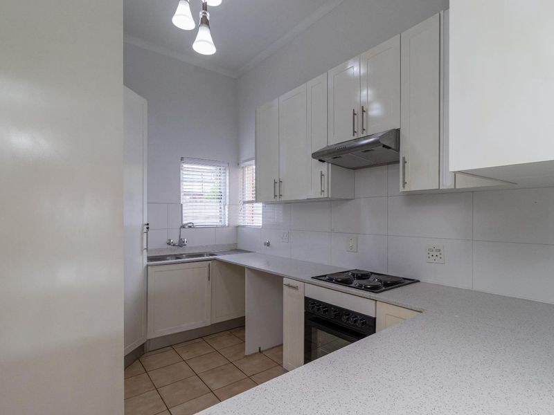 A clean and functional kitchen featuring white cabinetry, laminate countertops, a built-in oven with hob, and tiled finishes throughout.