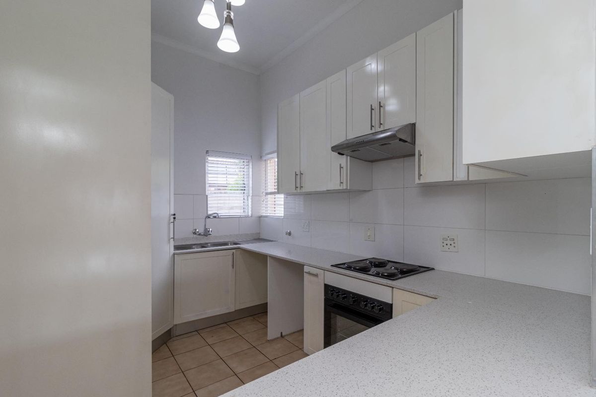 A clean and functional kitchen featuring white cabinetry, laminate countertops, a built-in oven with hob, and tiled finishes throughout.