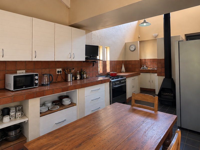 A rustic kitchen featuring tiled countertops, built-in cabinetry, a freestanding fireplace, and a skylight, offering a functional space with potential for modern updates.