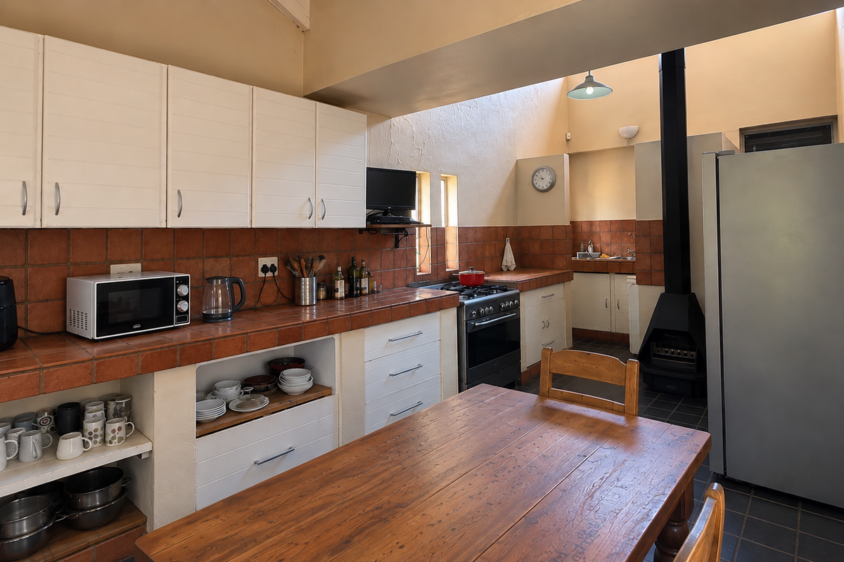 A rustic kitchen featuring tiled countertops, built-in cabinetry, a freestanding fireplace, and a skylight, offering a functional space with potential for modern updates.