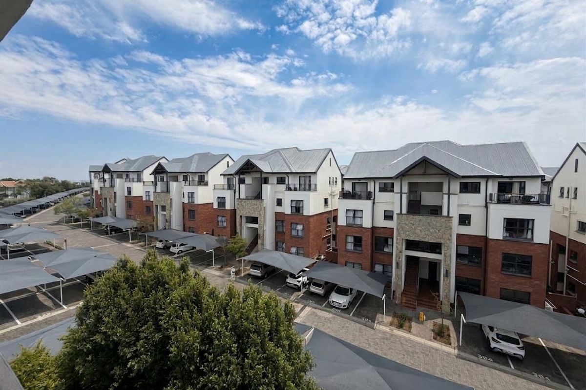 An elevated aerial view of a modern apartment complex featuring brick and plaster facades, metal roofing, and designated covered parking areas.