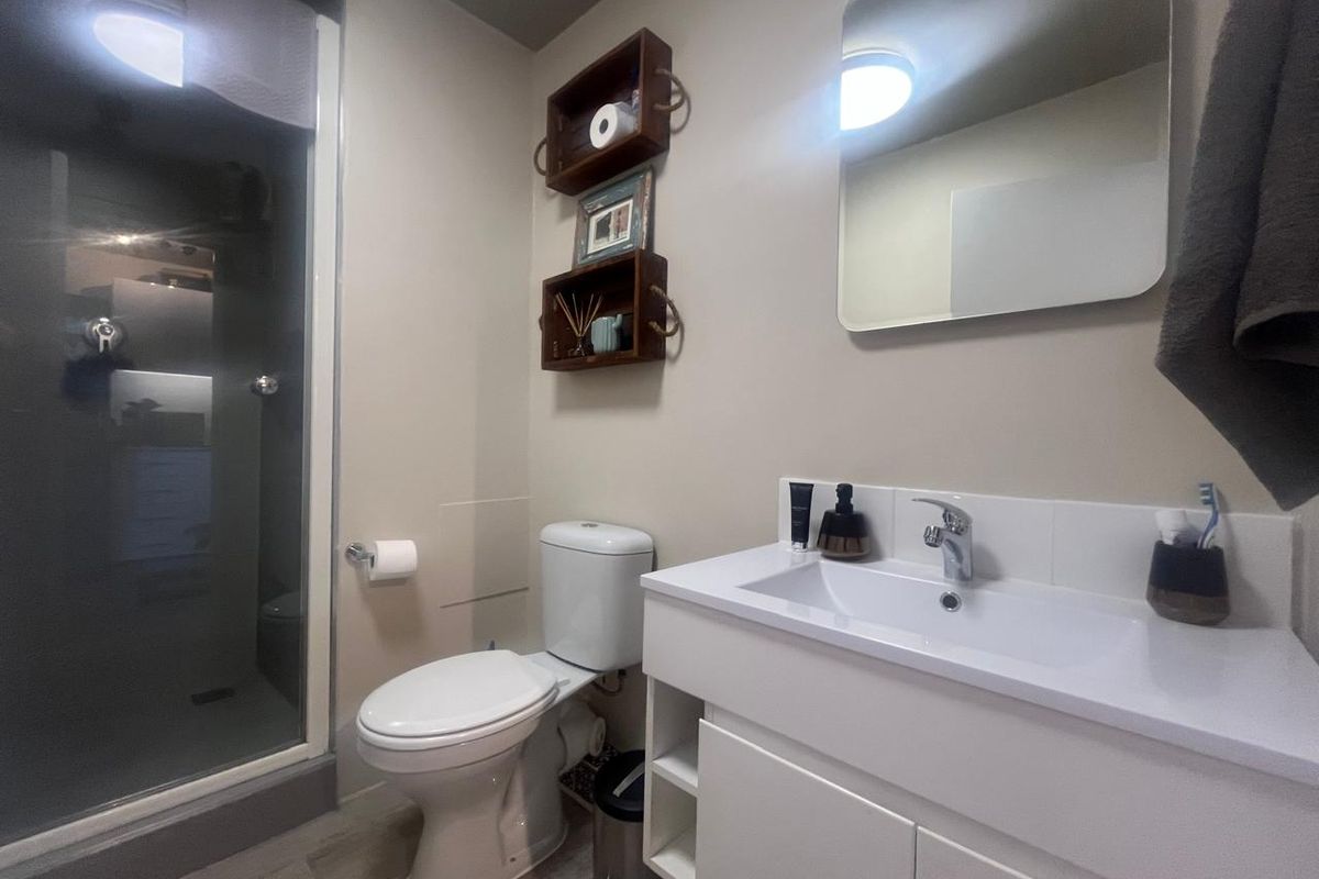 A modern, well-maintained bathroom featuring a glass shower enclosure, a white vanity unit with integrated basin, and a wall-mounted mirror.