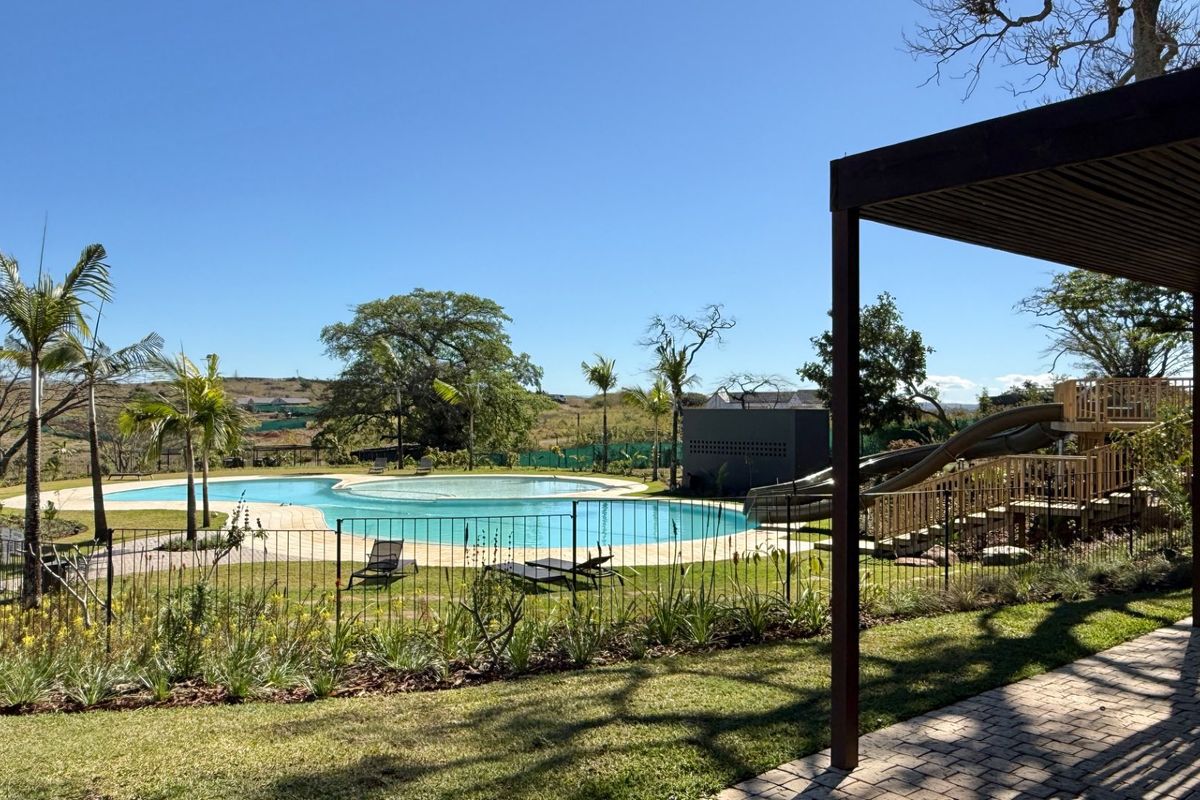 A well-maintained outdoor pool area featuring a swimming pool, paved patio, pergola, and playground equipment set within a landscaped garden.