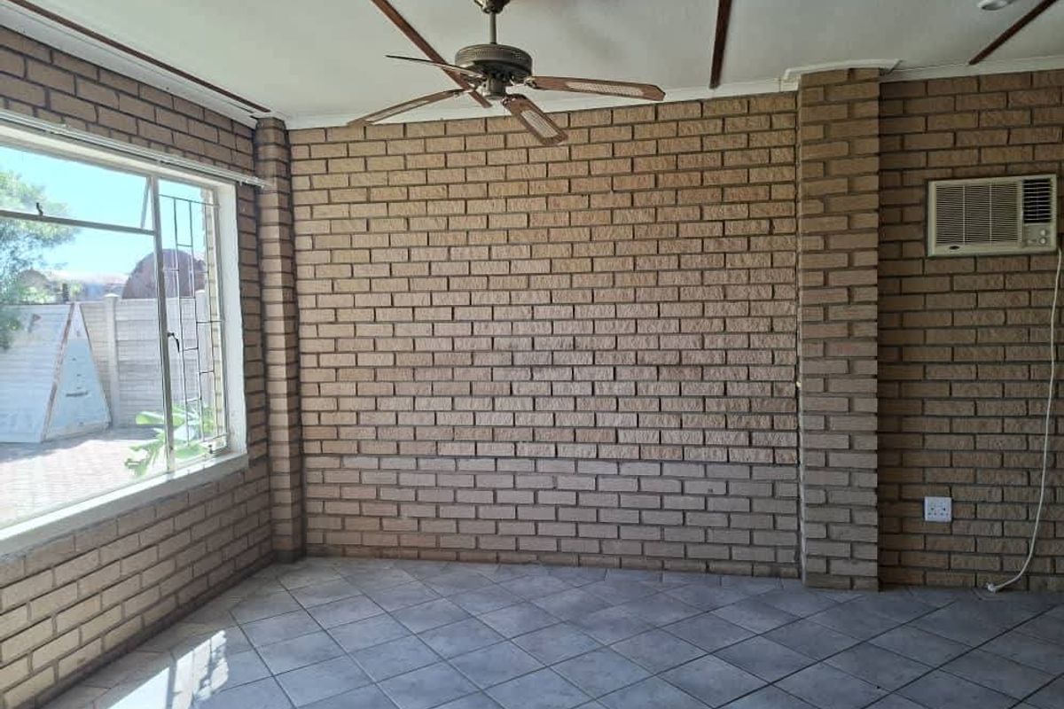 An empty living area featuring exposed brick walls, tiled flooring, a ceiling fan, and a wall-mounted air conditioning unit.