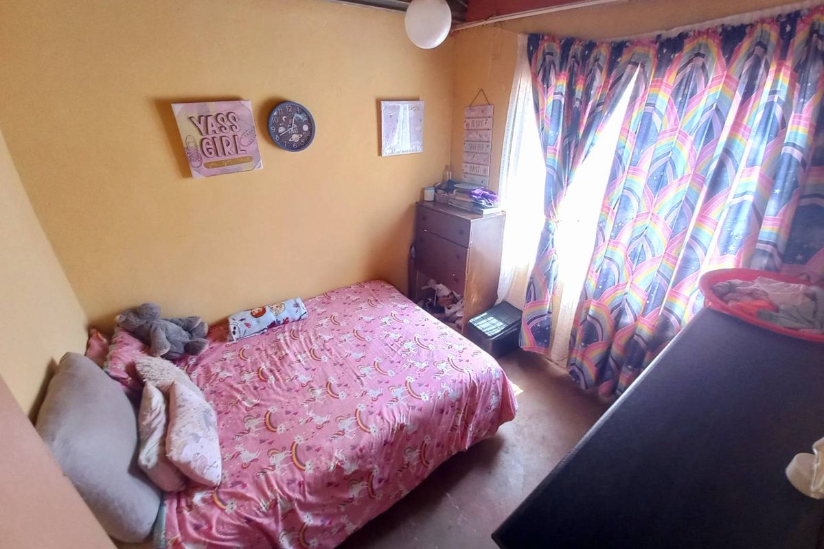 A bedroom featuring yellow painted walls, a window with curtains, and exposed ceiling beams.