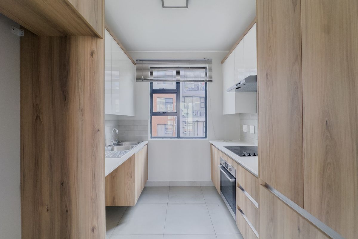 A modern, galley-style kitchen featuring light wood-grain cabinetry, white high-gloss upper cabinets, integrated appliances, and neutral floor tiles.