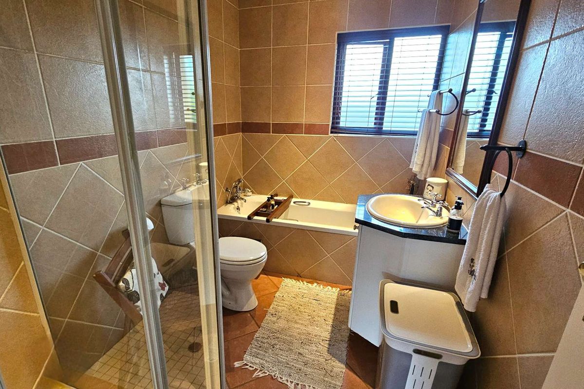 A functional bathroom featuring a built-in bathtub, separate glass-enclosed shower, vanity basin, and tiled walls and flooring.