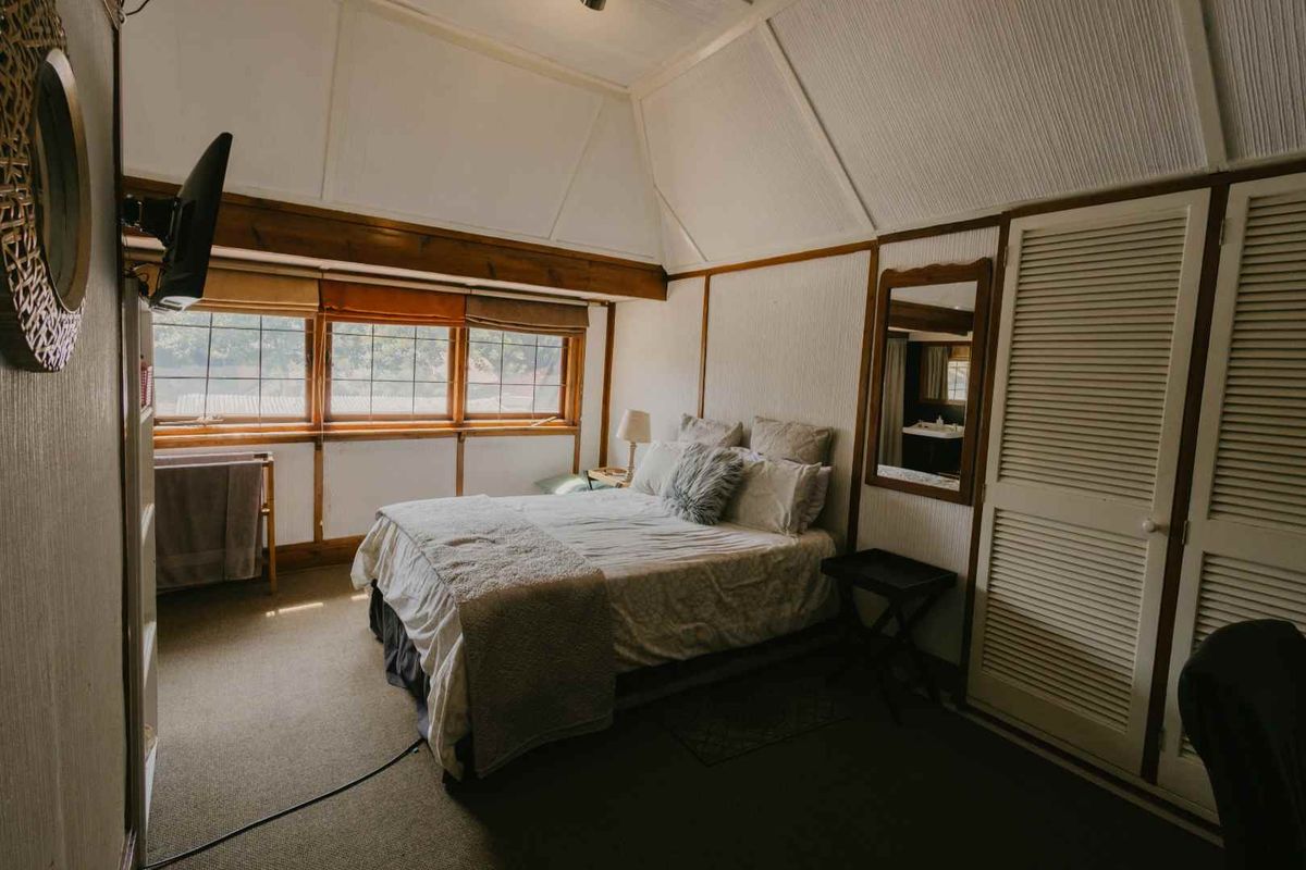A bedroom featuring a vaulted ceiling, built-in louvered closet doors, and large windows with wooden frames, offering a cozy and traditional aesthetic.