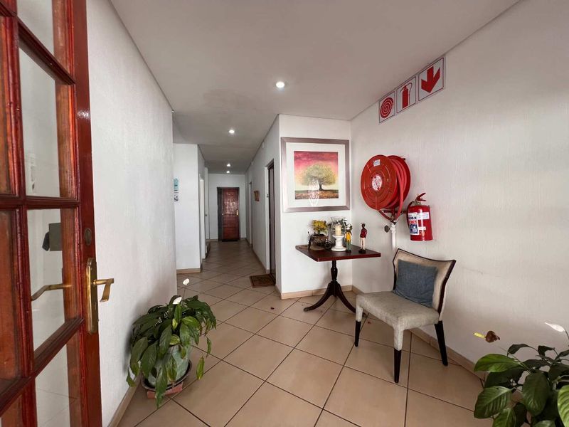 A functional apartment hallway featuring tiled flooring, recessed lighting, and essential fire safety equipment including a hose reel and extinguisher.