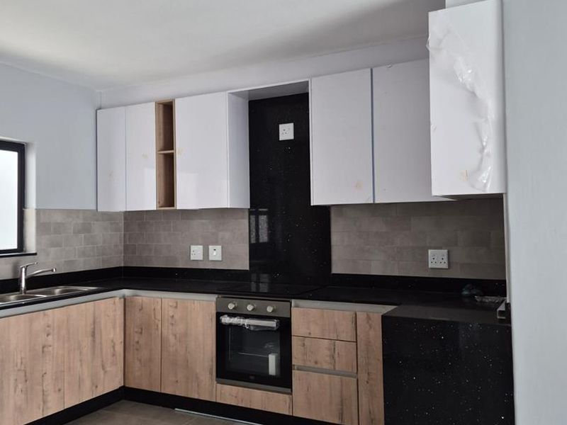 Modern kitchen featuring wood-grain and white cabinetry, black granite countertops, built-in oven, hob, and tiled backsplash in a clean, contemporary finish.