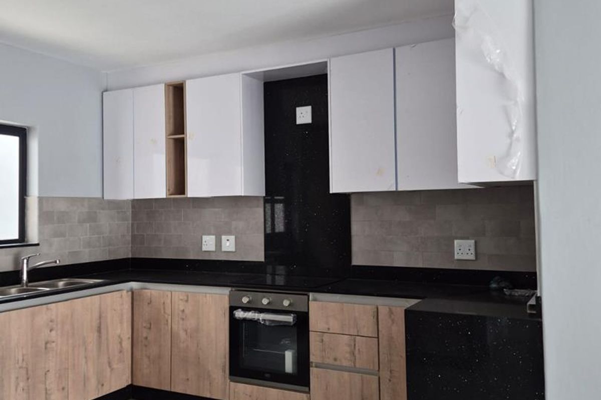 Modern kitchen featuring wood-grain and white cabinetry, black granite countertops, built-in oven, hob, and tiled backsplash in a clean, contemporary finish.