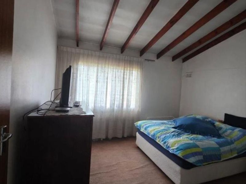 A bedroom featuring exposed timber ceiling beams and carpeted flooring, offering a functional space with potential for cosmetic updates.