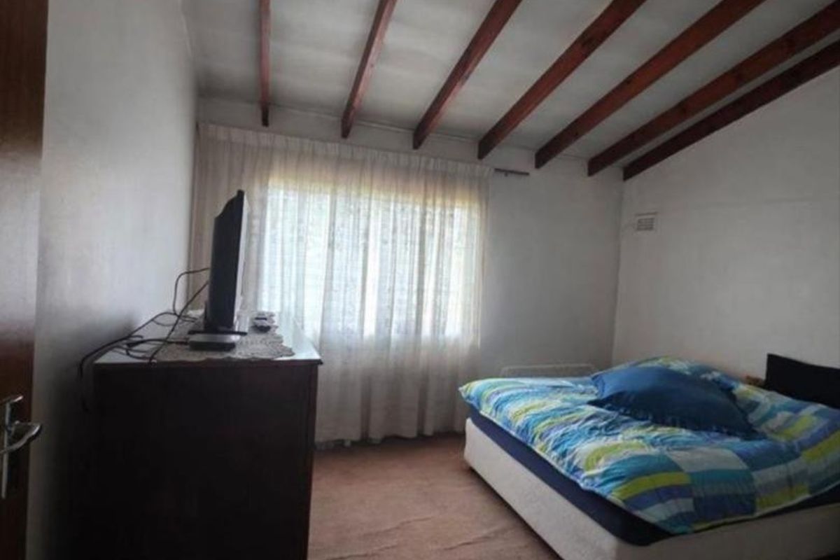 A bedroom featuring exposed timber ceiling beams and carpeted flooring, offering a functional space with potential for cosmetic updates.