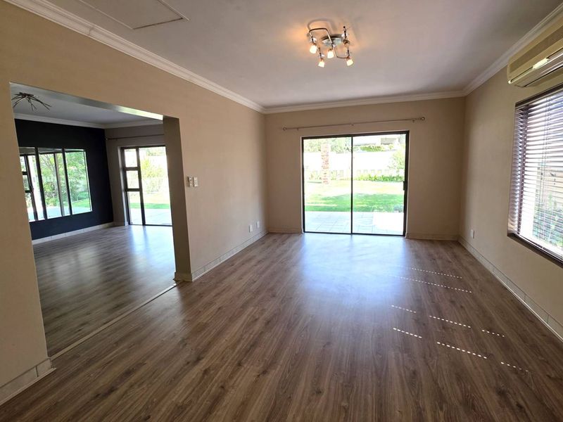 Spacious, light-filled living area featuring laminate flooring, wall-mounted air conditioning, and large sliding glass doors providing direct access to the rear garden.